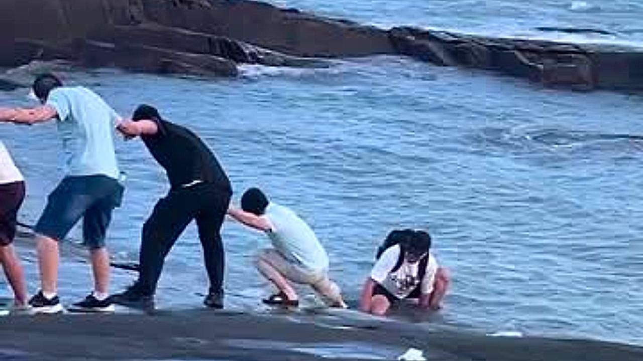 Video: Tourists form human chain to pull man stranded on slippery sea rocks to safety in China
